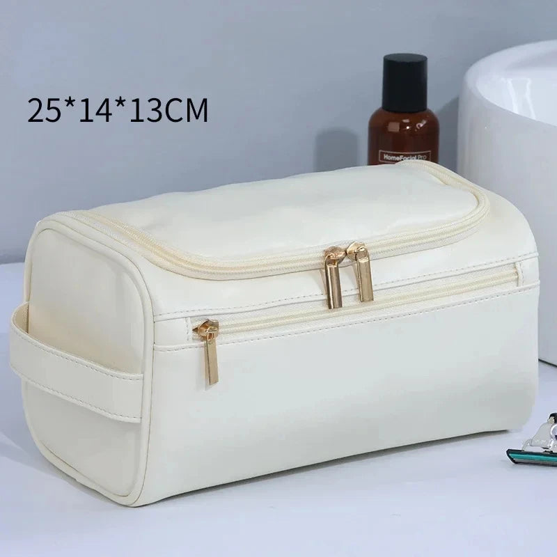 A cream-colored hanging leather toiletry bag with a zipper and brass hardware is shown on a white surface.