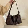 A woman holds a dark brown retro PU leather underarm bag against a light background.