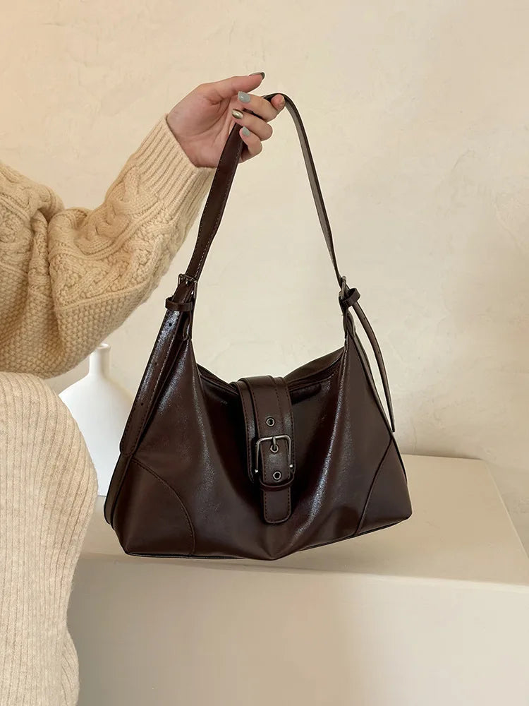 A woman holds a dark brown retro PU leather underarm bag against a light background.