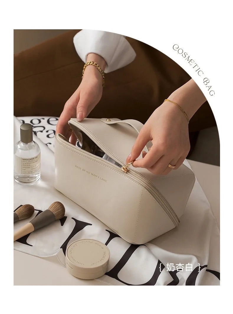 A beige foldable cosmetic storage bag is being held by a hand, next to a glass bottle and a makeup brush.