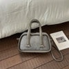 A light gray retro crocodile textured mini crossbody bag resting on a wooden floor next to a product card.