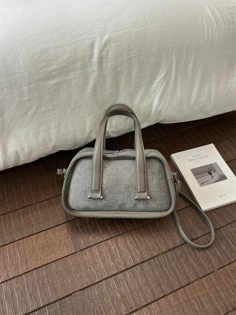 A light gray retro crocodile textured mini crossbody bag resting on a wooden floor next to a product card.
