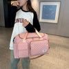 A woman holds a pink quilted portable travel duffle bag with tan straps in an indoor setting.