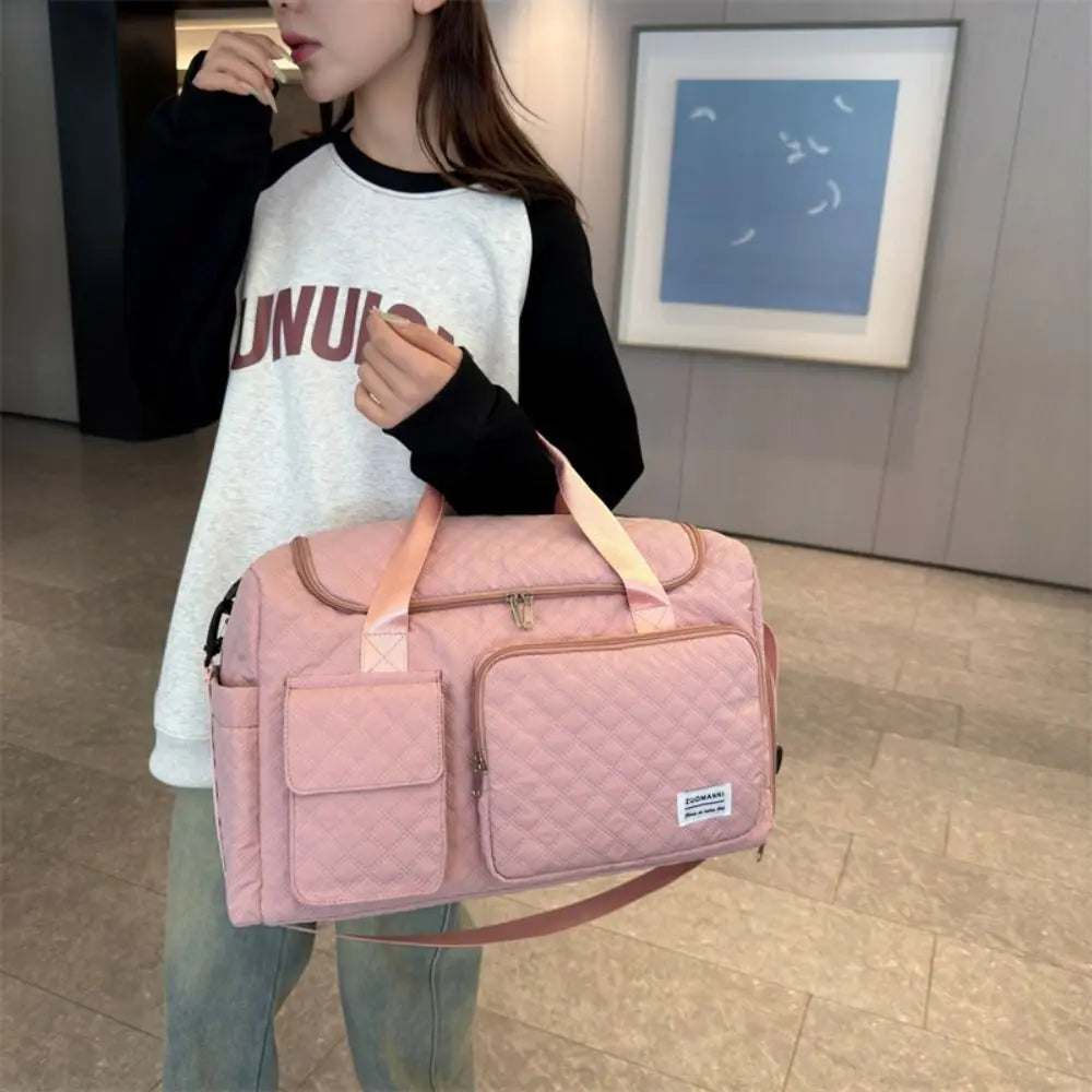 A woman holds a pink quilted portable travel duffle bag with tan straps in an indoor setting.