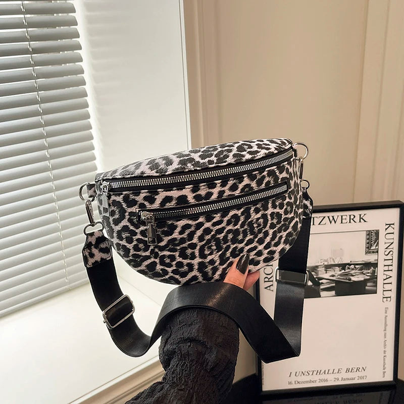 A woman holds a black leopard print PU leather crossbody bag with an adjustable strap in a bright room.
