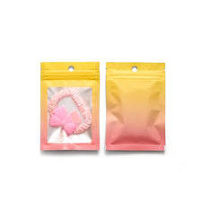 Two resealable gradient storage bags, one pink and yellow, containing jewelry or supplies.