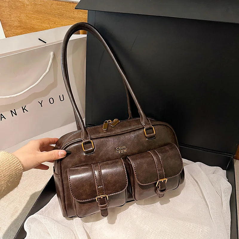A brown leather vintage letter print crossbody bag with gold hardware resting on a white surface.