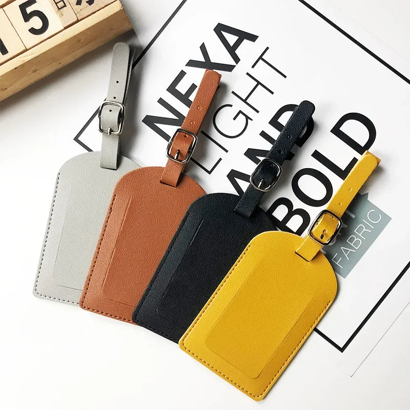 A collection of five PU leather luggage tags in various colors including gray, brown, black, and yellow, displayed on a white