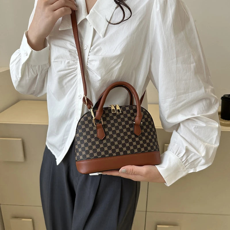 A woman holds a brown leather fashion shell shoulder crossbody bag with a checkered pattern against a light background.