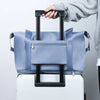 A hand is lifting a light blue expandable travel organizer bag from a white suitcase.