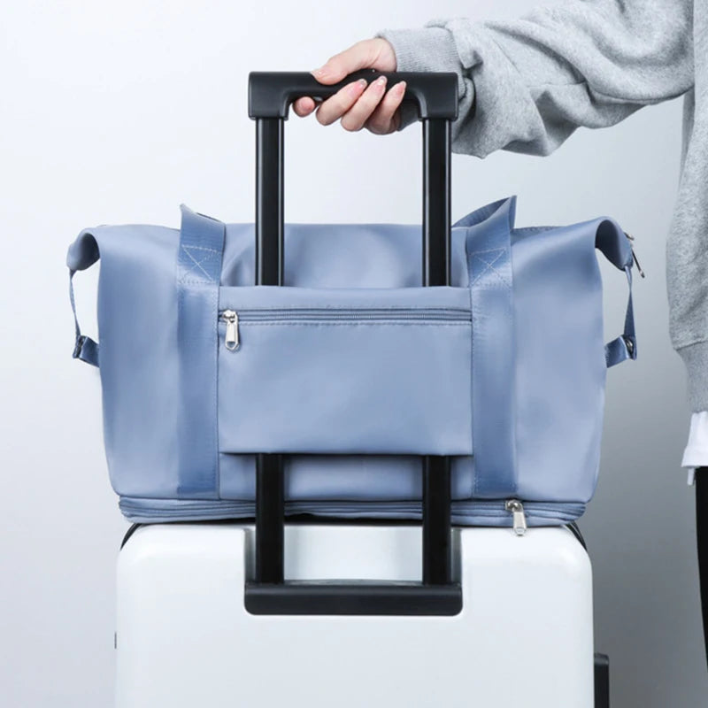 A hand is lifting a light blue expandable travel organizer bag from a white suitcase.