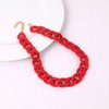 A red acrylic statement choker necklace with a gold-tone clasp is displayed on a white surface.