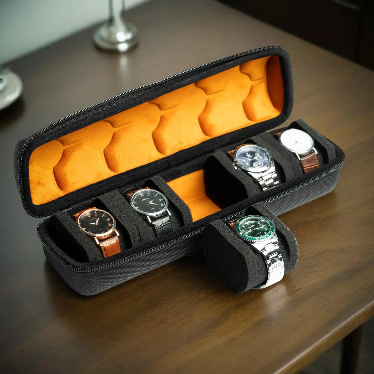 A black watch organizer case with an orange soft lining displaying several wristwatches.