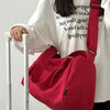 A person holds a bright red canvas crossbody travel tote bag in front of a white shirt.