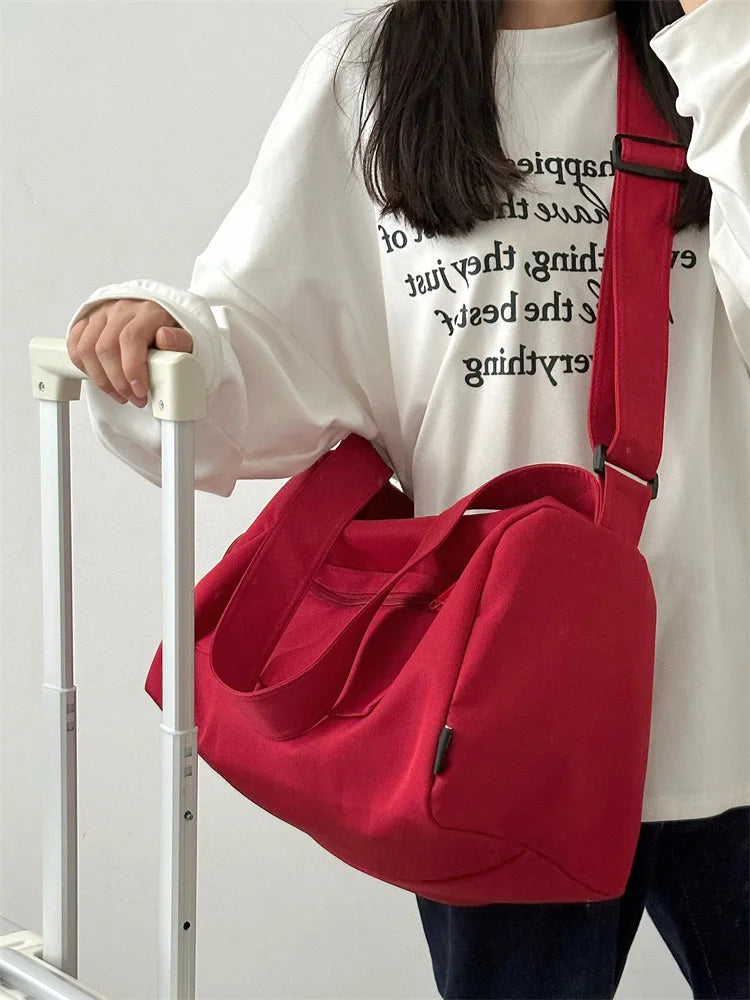 A person holds a bright red canvas crossbody travel tote bag in front of a white shirt.