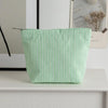 Clutch de rayas verde claro sobre una superficie blanca junto a una foto enmarcada.