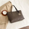 A brown faux leather letter-print tote bag with a leather handle rests next to a light beige blazer and a white cup.