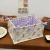 A quilted cotton storage basket with a white background and purple checkered lining, featuring lace flower designs.
