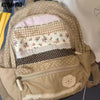 A beige backpack with a layered fabric front featuring floral prints and checkered patterns.