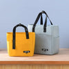 A yellow insulated lunch tote bag and a gray insulated lunch bag are displayed on a wooden surface.