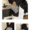 A woman holds a black shirt and white pants, displaying a striped black and white crochet handbag.
