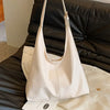 A light beige PU leather slouchy hobo shoulder bag is being held over a black leather couch.