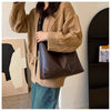 Eine Frau trägt einen beigen Strickcardigan und Jeans und hält eine braune Leder-Tasche.