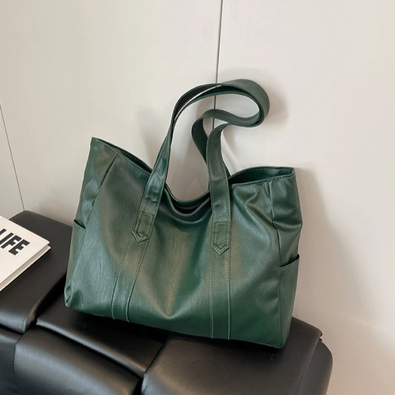 A dark green vintage-style zip-top tote bag made of durable vegan leather resting on a black surface.