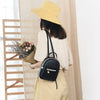 A woman wearing a yellow hat and beige top carries a black waterproof PU mini backpack.