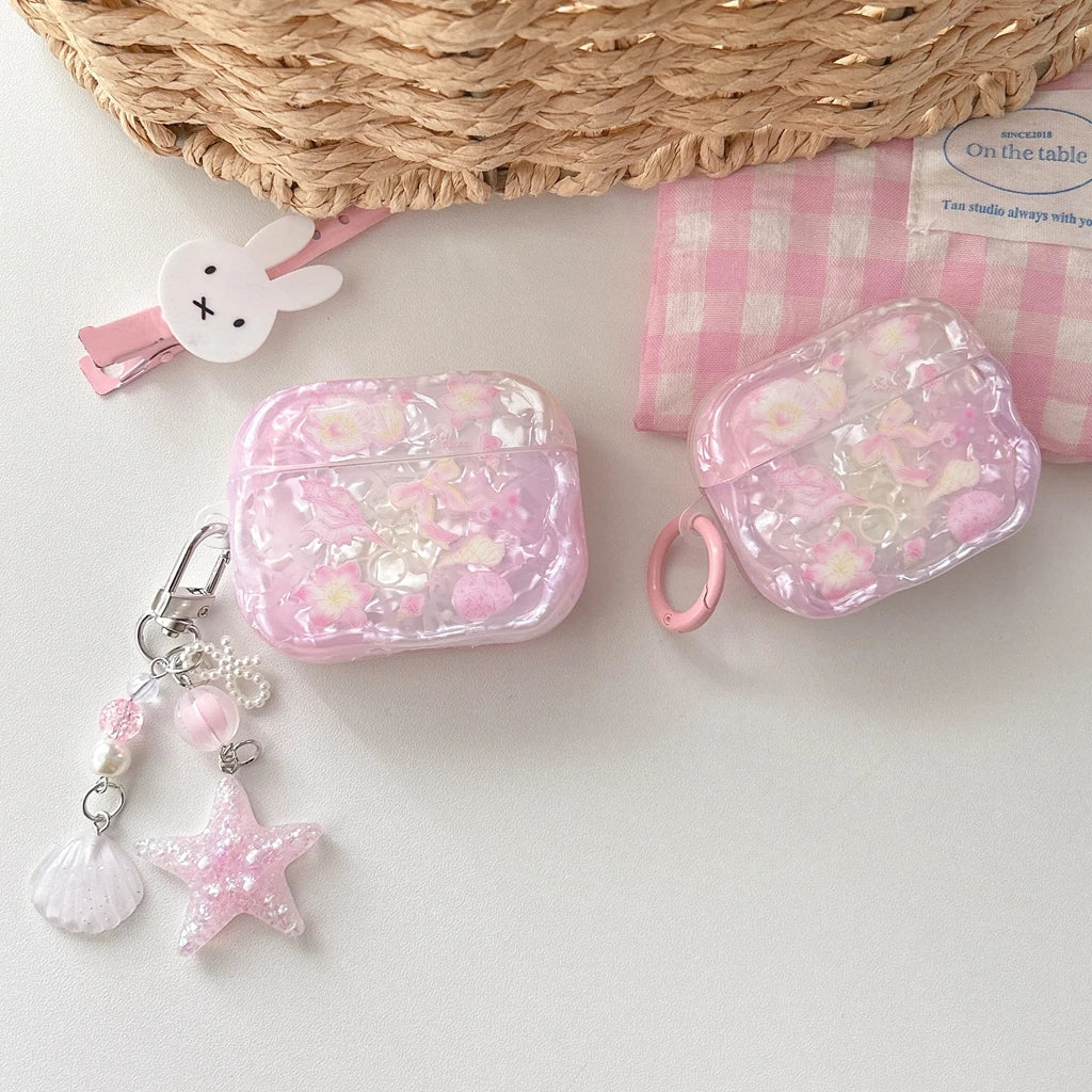 Étui d'écouteurs AirPods avec nœud floral rose, présenté sur une surface blanche à côté d'un tissu à carreaux roses et d'un p