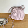 A light pink PU leather pleated crossbody bag with a matching strap resting on a wooden surface.
