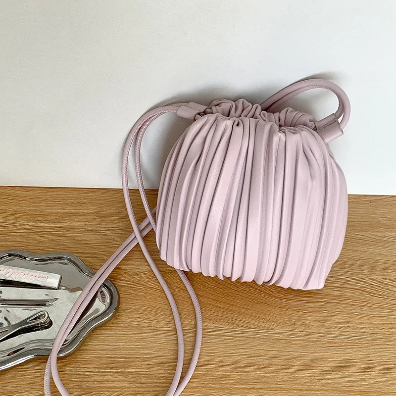 A light pink PU leather pleated crossbody bag with a matching strap resting on a wooden surface.