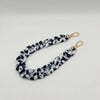 A close-up of a black and white woven acrylic chain bracelet with gold-colored clasps.