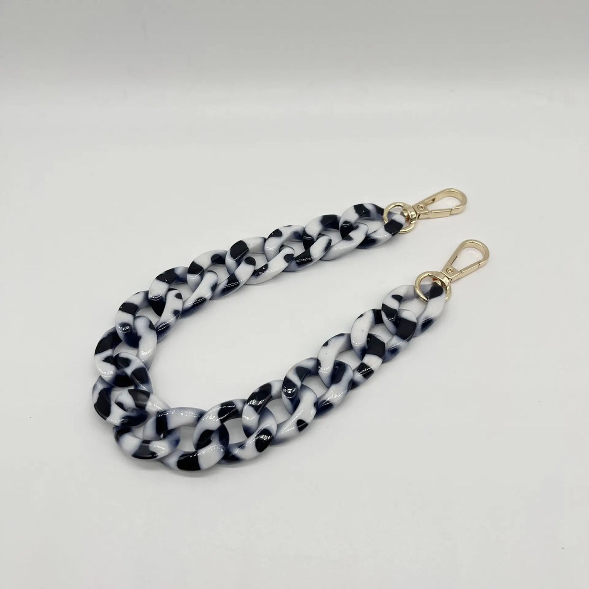A close-up of a black and white woven acrylic chain bracelet with gold-colored clasps.