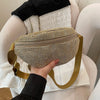A hand holds a gold-toned, rhinestone-embellished beige crossbody waist bag with a matching strap.