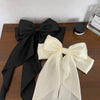 A black silk bow tied in a large bow shape next to a cream colored silk bow.