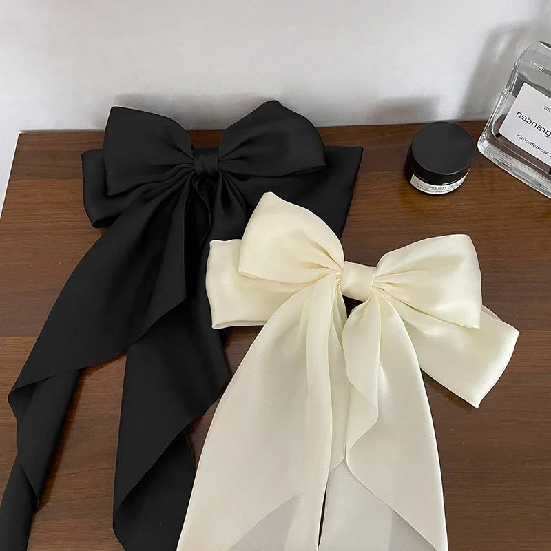 A black silk bow tied in a large bow shape next to a cream colored silk bow.