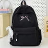 A black portable embroidered backpack with a white bow and decorative tassels is shown on a white surface.
