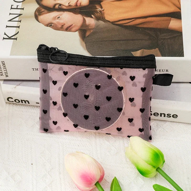 A pink mesh cosmetic storage pouch with a black zipper and elastic closure resting on a white surface.