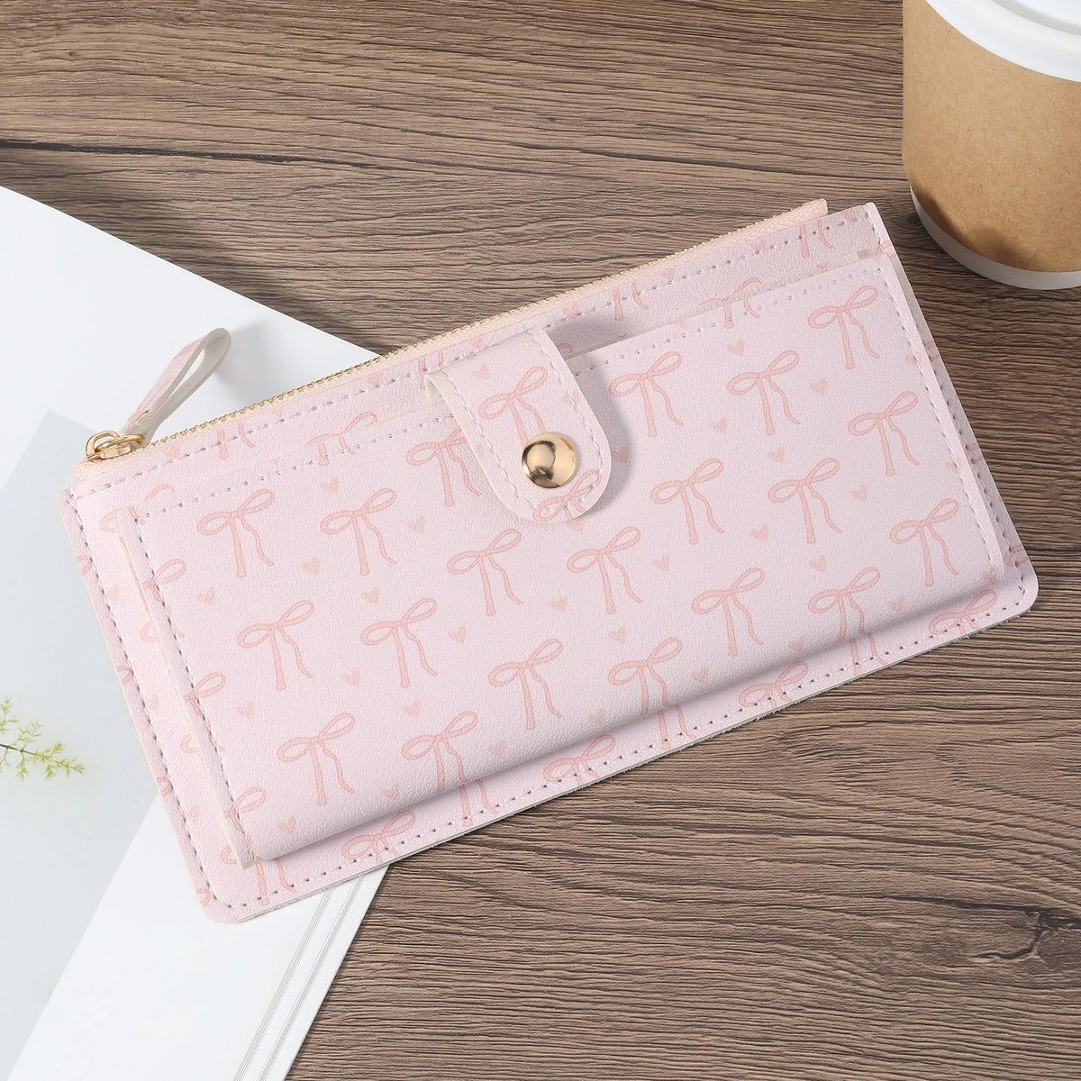 A pink elegant folding multi-card wallet with a zipper and decorative bows resting on a wooden surface.