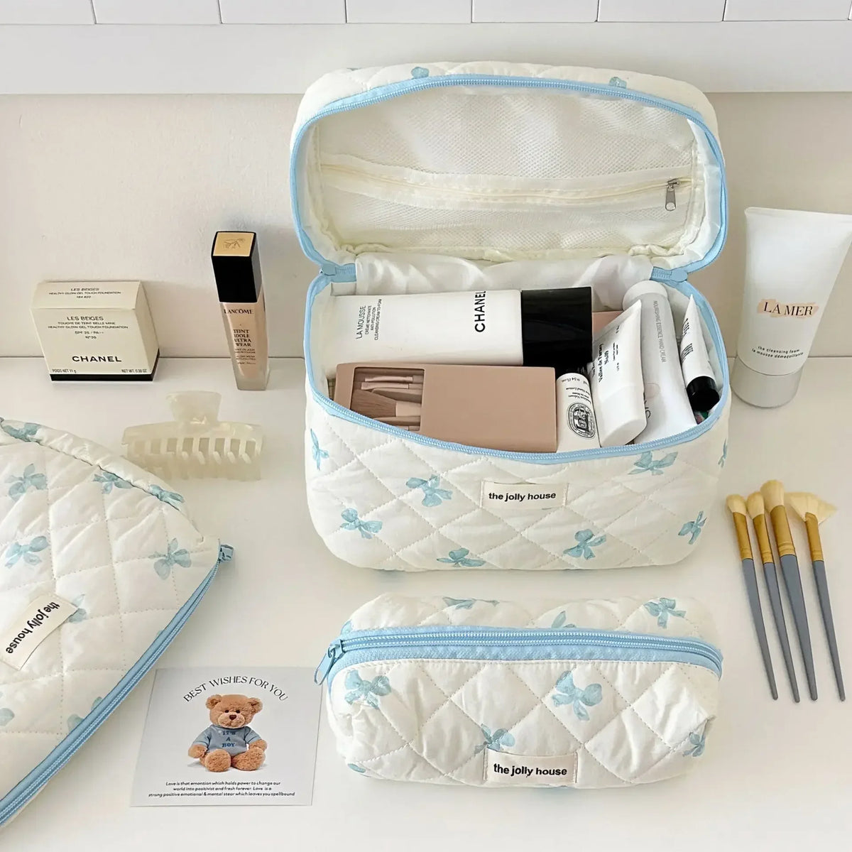 Sac de rangement cosmétique en matelassé blanc avec bordure bleue, ouvert et montrant les produits de maquillage à l'intérieu