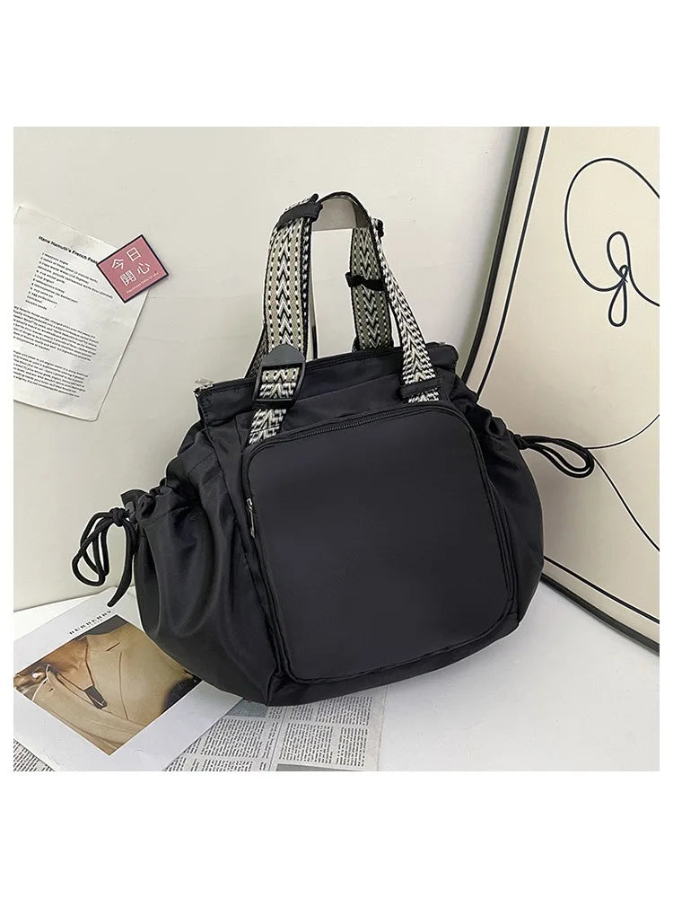 A black nylon shoulder bag with patterned straps is shown next to some papers and a notebook.