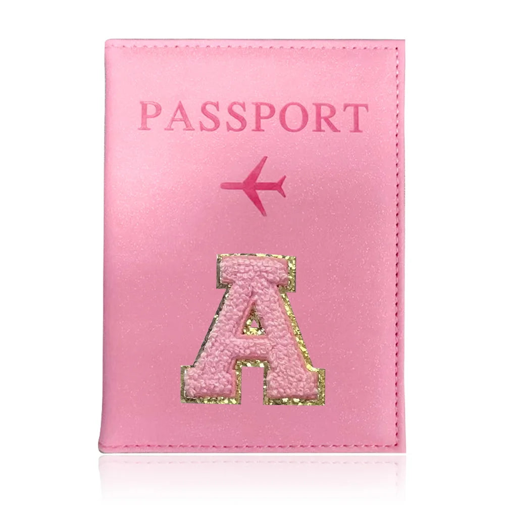 A pink leather passport holder with a gold initial A embossed on the cover.