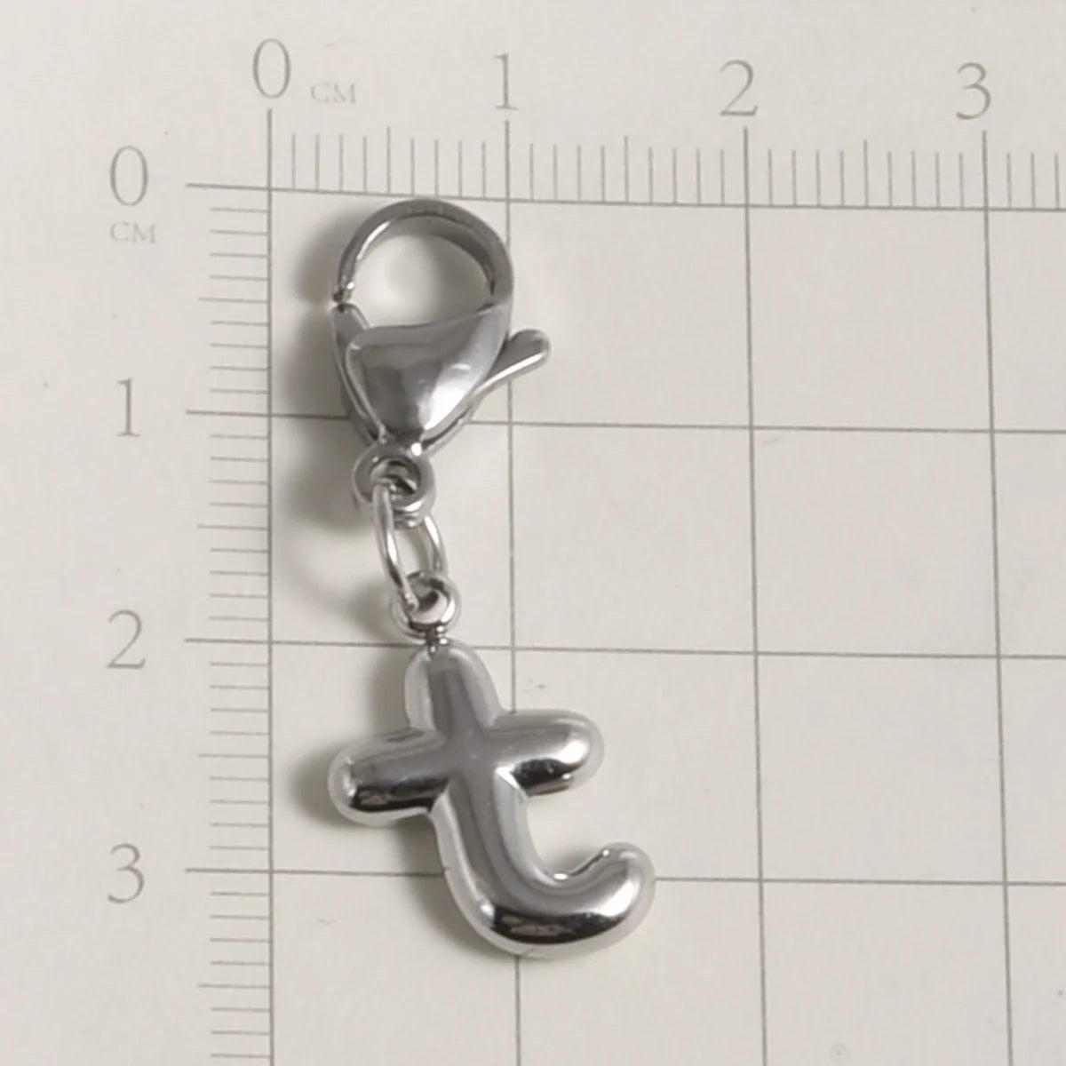 Silver stainless steel alphabet letter charm with a lobster clasp placed on a ruler for scale.