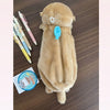 A fluffy brown otter plush pencil case with a zipper and a light blue tag is shown on a wooden surface.