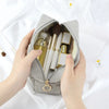 A hand opens a gray corduroy makeup organizer bag revealing various cosmetic brushes and products.