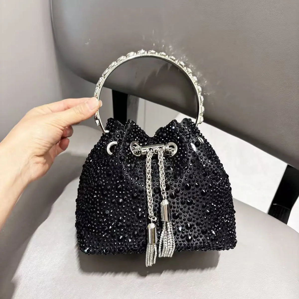 A black crystal-embellished evening clutch with a silver chain and hoop is held by a hand.