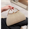 A hand holds a beige pleated glitter evening handbag with a gold top handle and chain strap against a dark background.