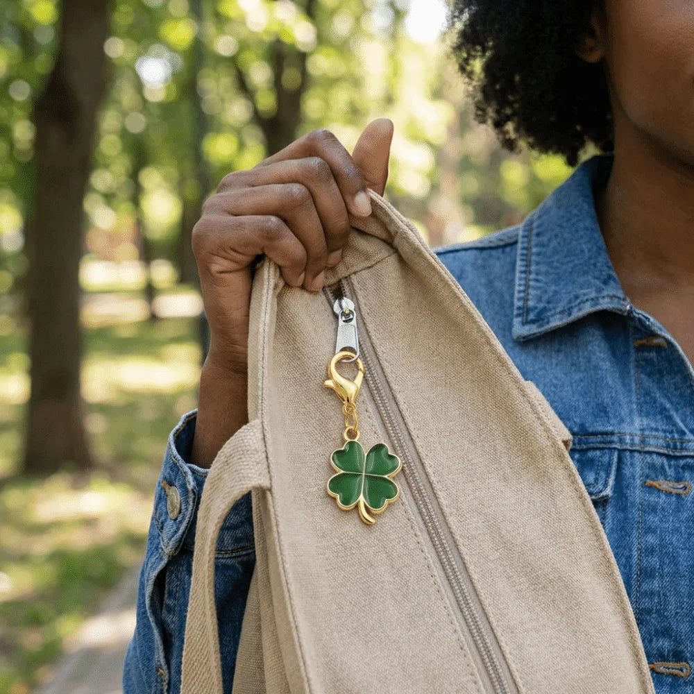 A person holds a tan canvas bag with a gold four-leaf clover keychain attached to the zipper.