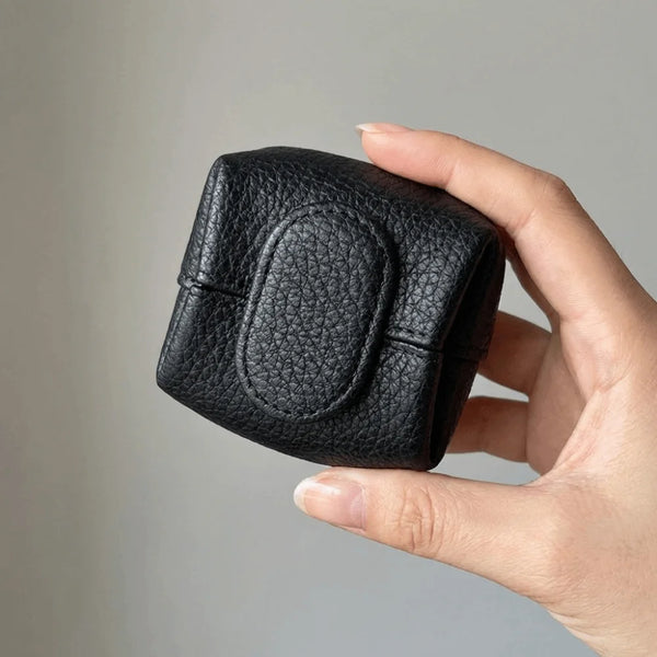 A hand holds a black, rectangular coin purse with a textured finish and snap closure.